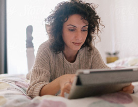Woman lying on bed looking at a tablet